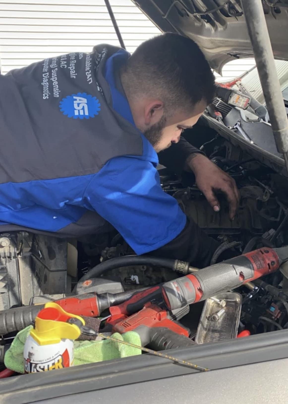 Andy working under the hood of a vehicle in his ASE-certified work shirt